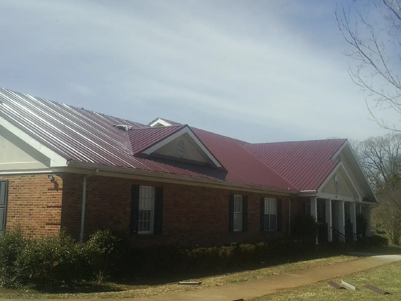 Red metal roof with gabled entries on a long brick building, from a Hail Damage Roof Repair job in Blandford