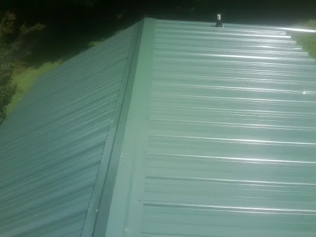 New green metal panels meeting at the ridge of a roof — Flat Roof Repair work by our crew in Blandford