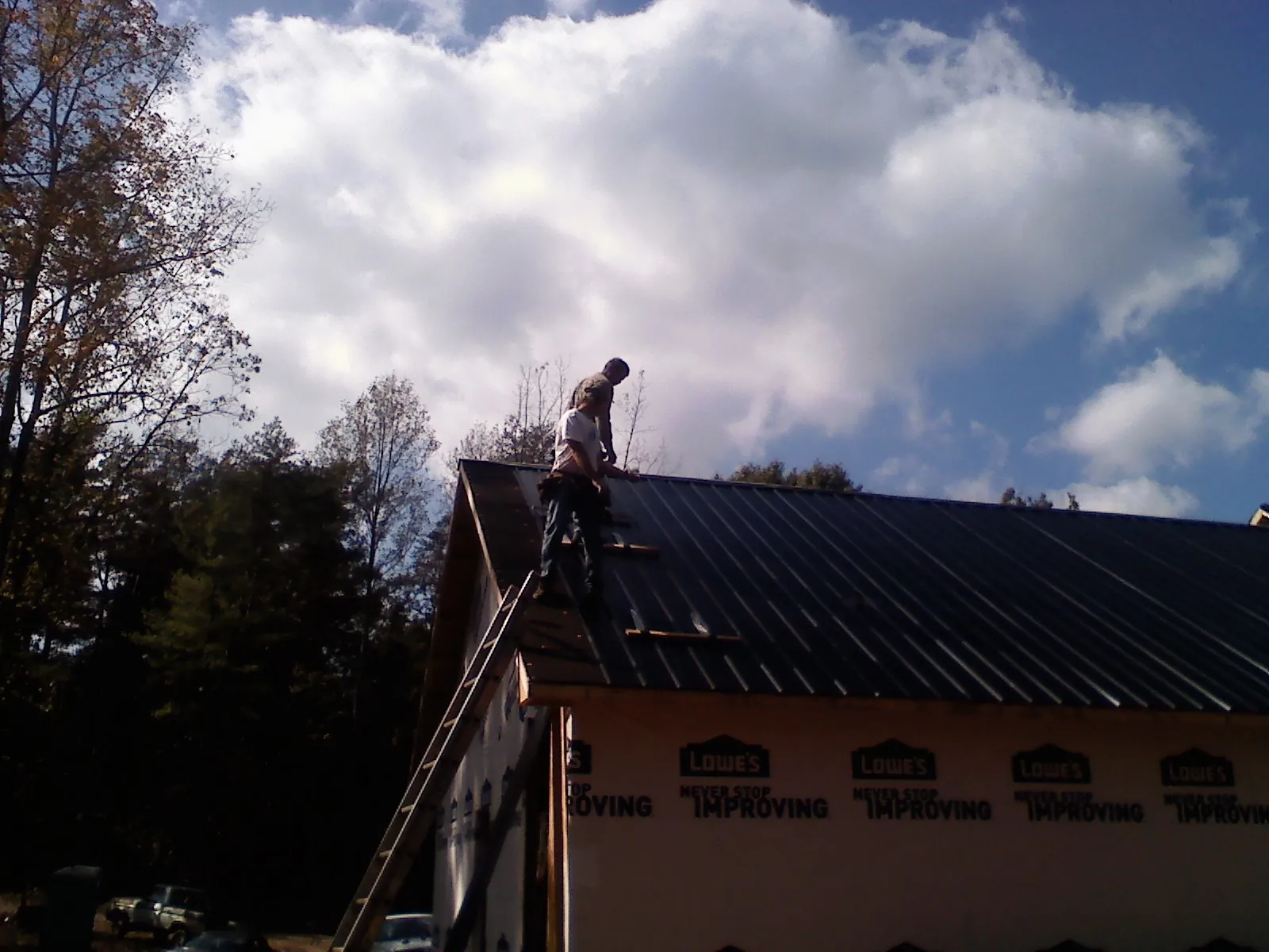 Roofer fastening dark metal panels high against a cloudy sky, from a Roof Inspection job in Blandford