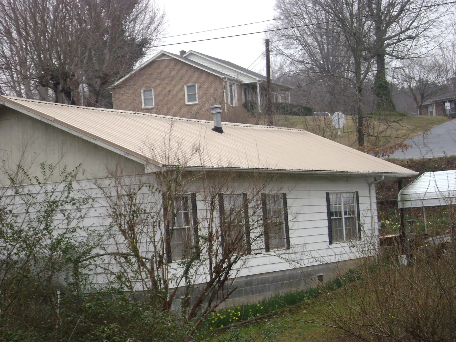 Tan metal roof on a white sided house set into a hillside — Commercial Roofing by Roofing Brothers in Blandford