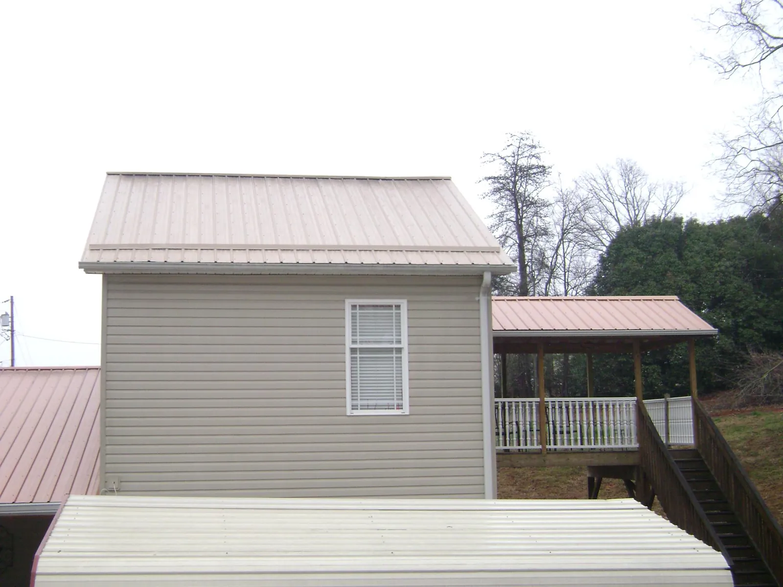 Tan metal roofs on a two story addition and attached porch, from a Roof Replacement job in Blandford